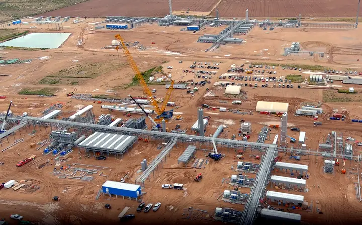 A wide plant site under construction, with pipe racks, equipment and a crawler crane, seen from the air