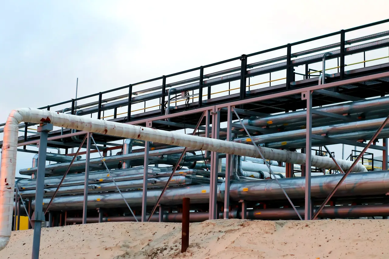 A steel pipe rack carrying rows of insulated process piping, against an evening sky